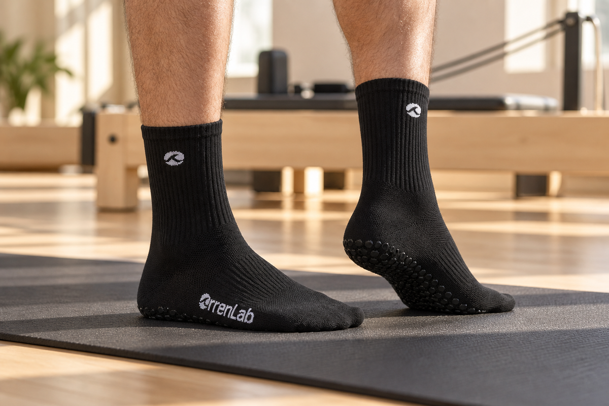 Black Orrenlab grip socks worn on a Pilates mat in a sunlit studio.